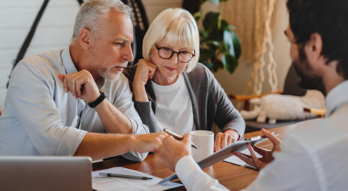 Financial advisor explaining paperwork to elderly retired couple front of desk