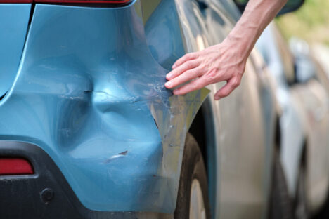 Driver hand examining dented car with damaged fender parked on city street side. Road safety and vehicle insurance concept Driver hand examining dented car with damaged fender parked on city street side. Road safety and vehicle insurance concept