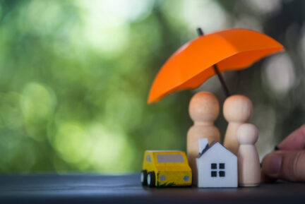 House, car and family sits safely under a orange umbrella, symbolizing home protection and security against life uncertainties.